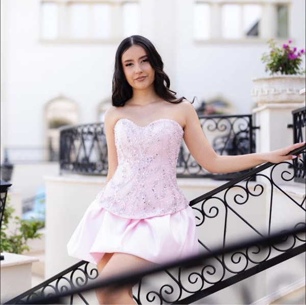 fata cu parul saten imbracata in rochie scurta roz se tine de o balustrara