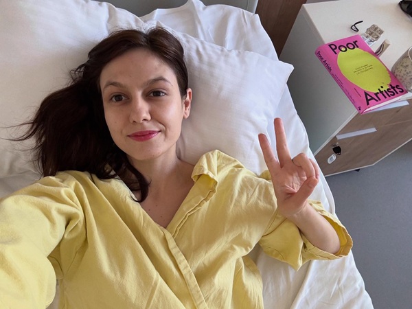 ada gales cu parul desprins imbracata in galben pe un pat de spital face semnul victoriei