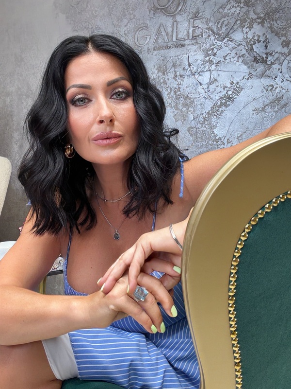 gabriela cristea cu parul mediu cu bucle sta pe un scaun imbracata in rochie bleu