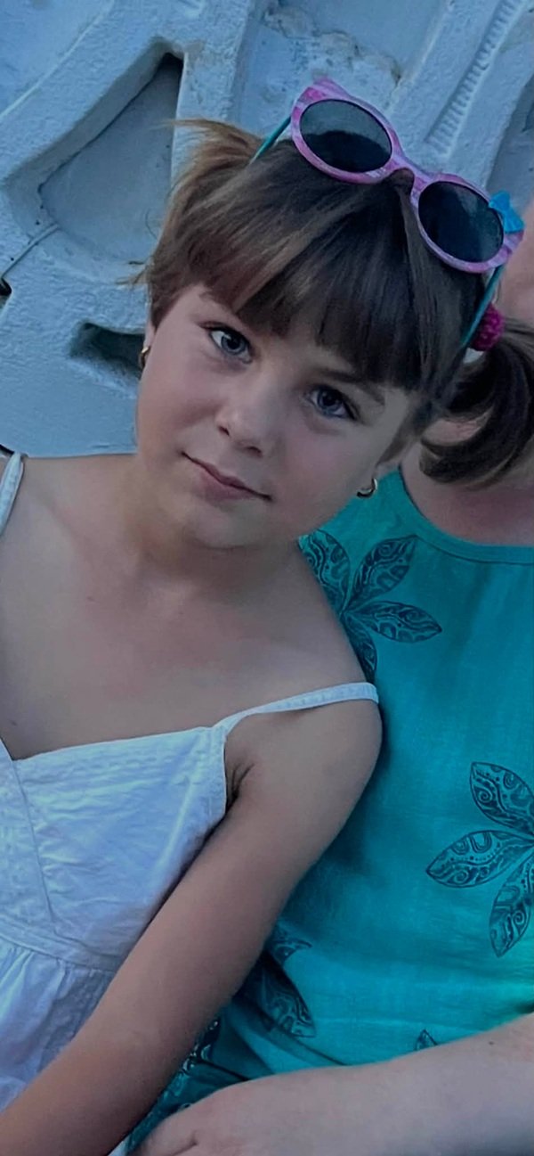 fetita in rochita alba cu doua codite zambeste la camera
