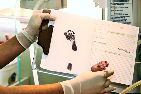 o asistenta asaza un piciorus de nou nascut pe o carte pentru a lasa o amprenta