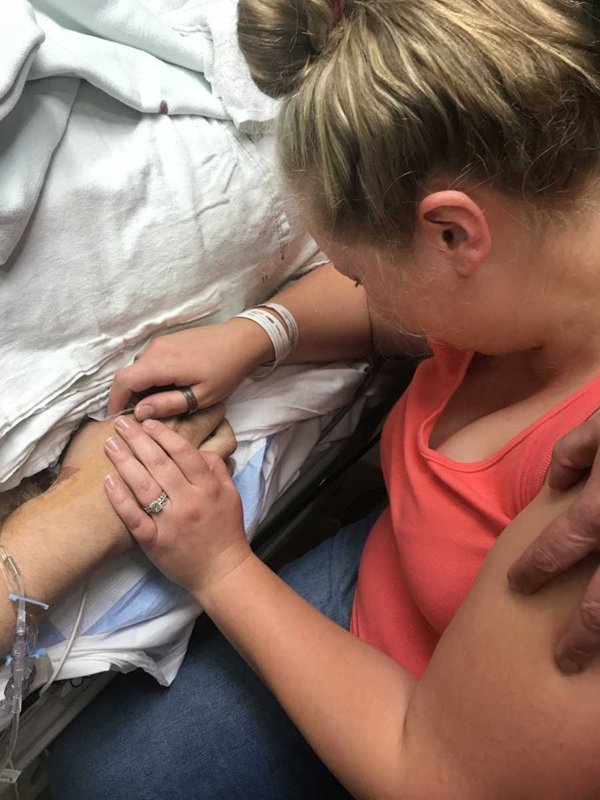 femeie plange langa patul de spital tinand o mana in mainile ei