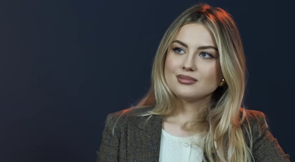femeie blonda cu parul lung imbracata in alb si sacou gri