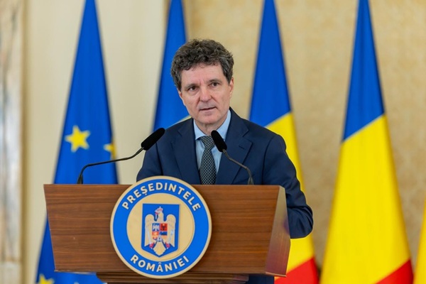 nicusor dan imbracat in costum albastru cu cravata la pupitru in spate steagul romaniei
