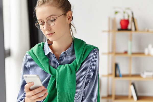 fata cu ochelari si o bluza verde legata se uita pe telefon