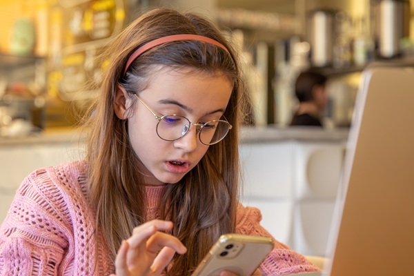 adolescenta imbracata in roz sta pe telefon la masa