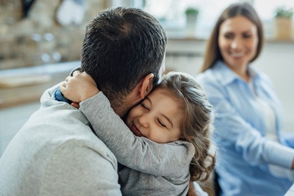 fetita in bluza gri isi tine tatal de gat si mama in camasa albastra ii priveste
