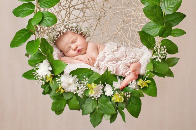 bebelus-care-doarme-sta-asezat-intr-un-leagan-din-lemn-si-are-pe-cap-o-coronita-din-flori-albe-iar-leaganul-este-decorat-cu-frunze-mari-verzi-si-flori-albe