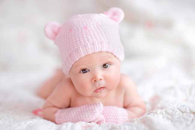 bebelus-fetita-care-sta-pe-burta-sprijinita-in-maini-are-manusi-roz-si-pe-cap-o-caciulita-roz
