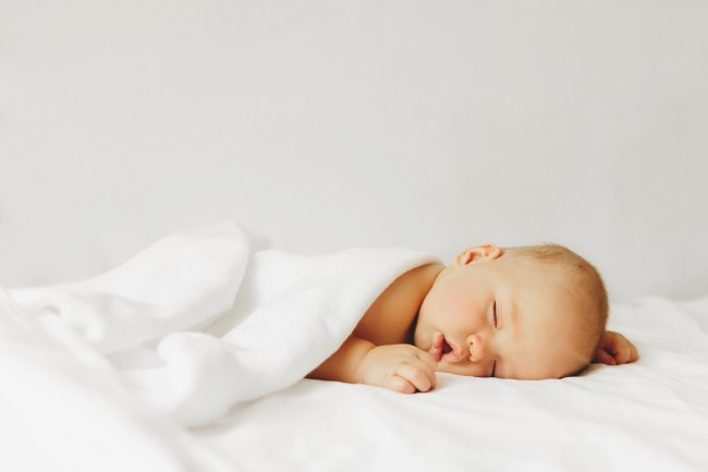 bebelus-care-doarme-cu-gura-deschisa-si-este-invelit-cu-o-patura-alba-si-sta-pe-un-pat-alb