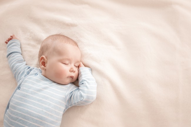 un-bebelus-in-body-bleu-cu-dungi-albe-doarme-pe-spate-cu-o-mana-sub-cap-si-alta-in-sus