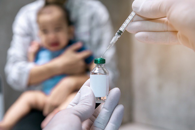 medic-care-extrage-cu-o-seringa-ser-pentru-vaccin-dintr-un-recipient-si-in-fundal-un-bebelus-care-este-tinut-in-brate