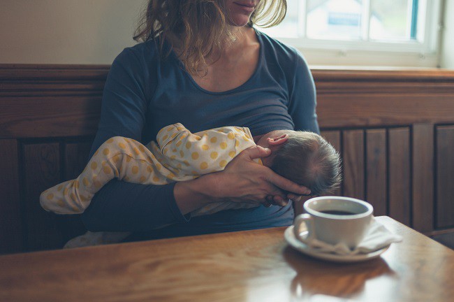 femeie-care-isi-alapteaza-copilul-si-are-o-ceasca-de-cafea-pe-masa-din-fata-ei
