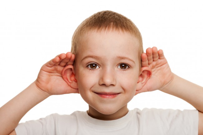 copil-care-zambește-și-își-ține-urechile-depărtate-de-cap